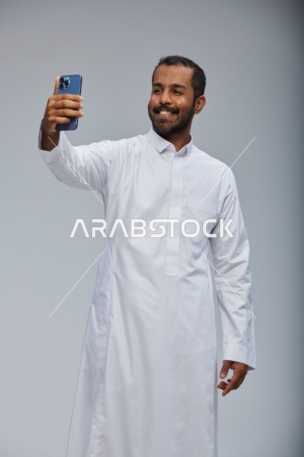 رجل سعودي بالثوب الأبيض يلتقط صورة سيلفي بالهاتف الذكي