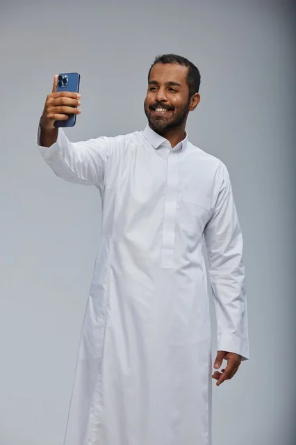 رجل سعودي بالثوب الأبيض يلتقط صورة سيلفي بالهاتف الذكي