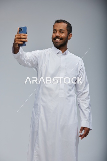 رجل سعودي بالثوب الأبيض يلتقط صورة سيلفي بالهاتف