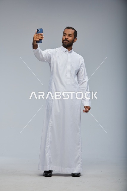 رجل سعودي بالثوب الأبيض يلتقط سيلفي بالهاتف الذكي