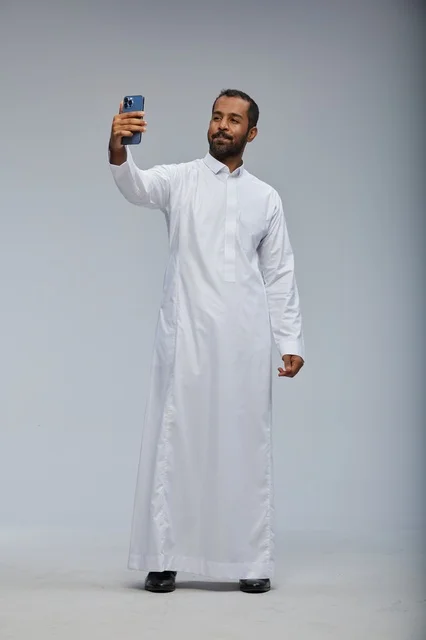 رجل سعودي بالثوب الأبيض يلتقط سيلفي بالهاتف الذكي