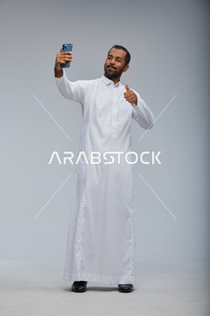 رجل سعودي بالثوب الأبيض يلتقط صورة سيلفي بالهاتف الذكي