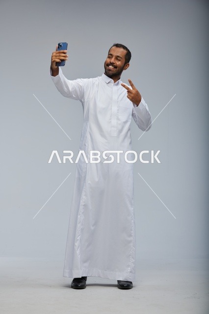 رجل سعودي يرتدي الثوب الأبيض يلتقط سيلفي بهاتف ذكي