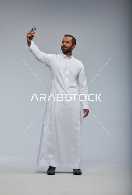 رجل سعودي بالثوب الأبيض يلتقط سيلفي بالهاتف الذكي