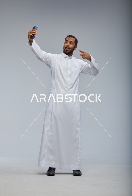 رجل سعودي بالثوب الأبيض يلتقط صورة سيلفي في استوديو