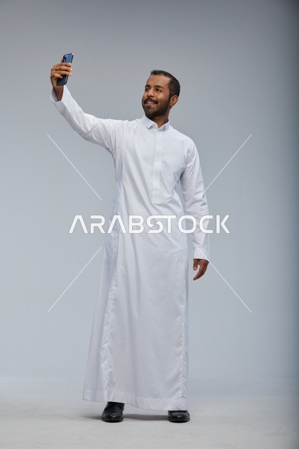 رجل سعودي بالثوب الأبيض يلتقط سيلفي بالهاتف