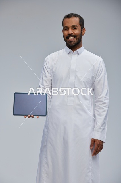 رجل سعودي بالثوب الأبيض يحمل جهاز لوحي