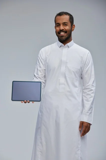 Saudi Man in White Thobe Holding Digital Tablet