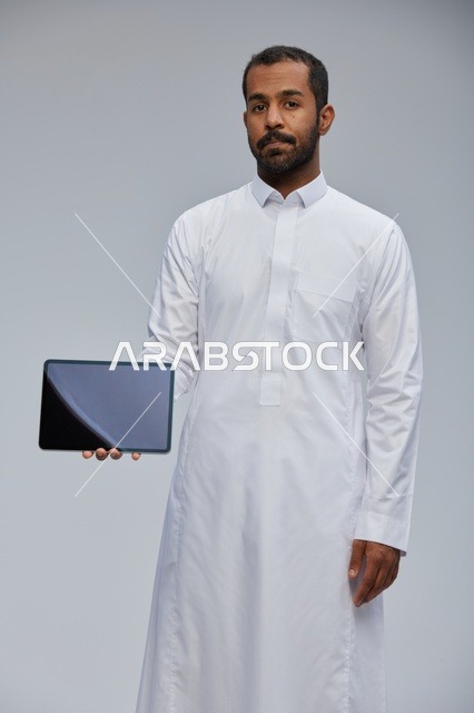 رجل سعودي بالثوب الأبيض يمسك بجهاز لوحي في الاستوديو