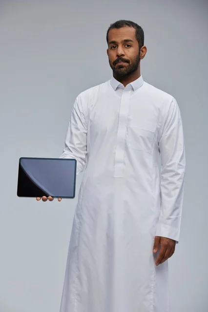 رجل سعودي بالثوب الأبيض يمسك بجهاز لوحي في الاستوديو