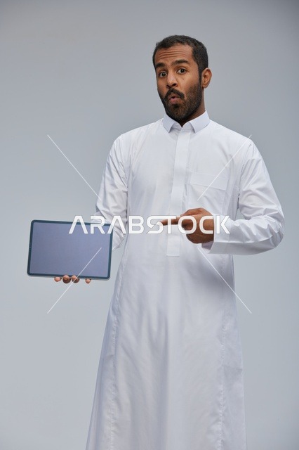 رجل سعودي بالثوب يشير إلى شاشة جهاز لوحي في الاستوديو