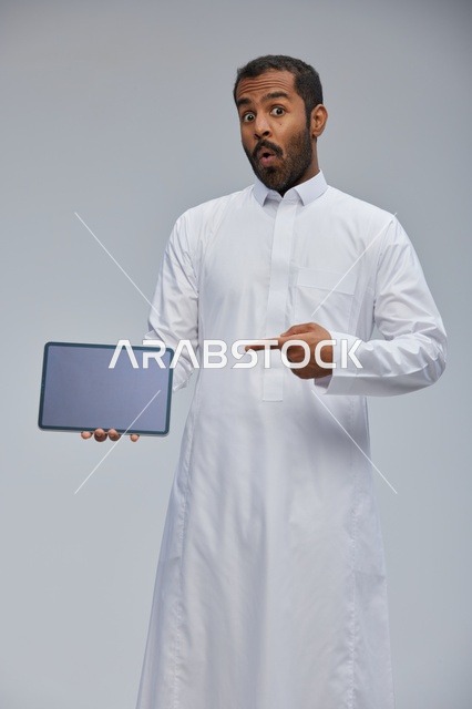 رجل سعودي بالثوب الأبيض يحمل جهازاً لوحياً
