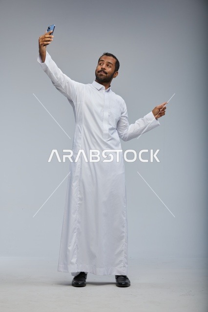 رجل سعودي بالثوب الأبيض يلتقط سيلفي بالهاتف الذكي