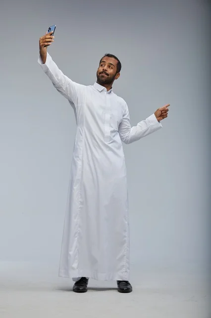 رجل سعودي بالثوب الأبيض يلتقط سيلفي بالهاتف الذكي