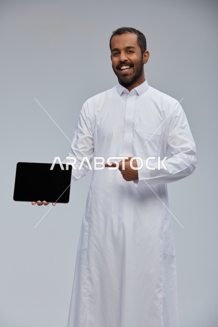 رجل سعودي بالثوب الأبيض يشير إلى شاشة جهاز لوحي
