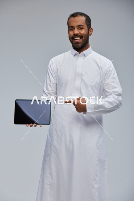 رجل سعودي بالثوب الأبيض يشير إلى جهاز لوحي
