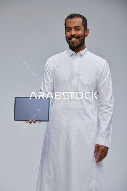 رجل سعودي بالثوب الأبيض يمسك جهازاً لوحياً