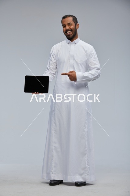 رجل سعودي بالثوب الأبيض يعرض جهاز لوحي في الاستوديو