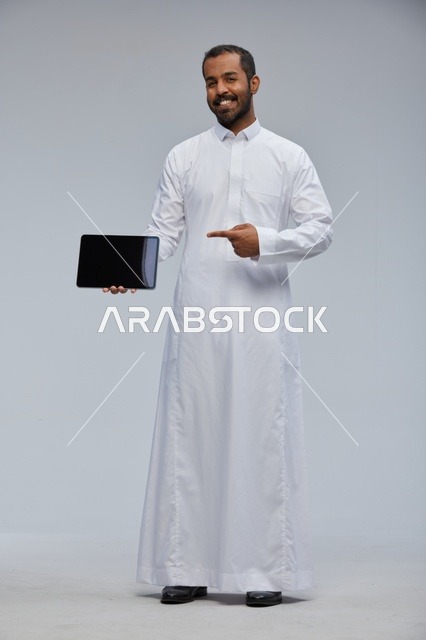 رجل سعودي بالثوب التقليدي يشير إلى جهاز لوحي