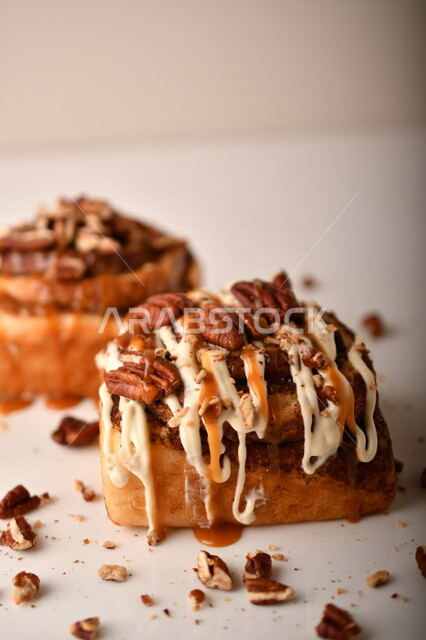 صورة مقربة للفائف القرفة اللذيذة المزينة بالجوز و الصوص الابيض، لفائف السينابون، معجنات، سينابون رول ، مخبوزات طازجة، لفائف الحلوى الشهية 