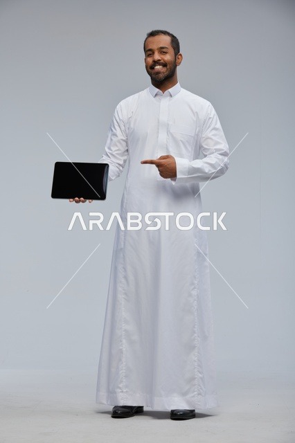 رجل سعودي بالثوب الأبيض يشير إلى جهاز لوحي رقمي