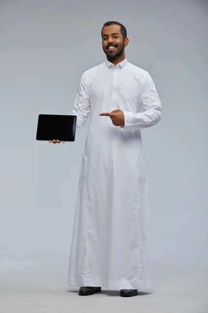 رجل سعودي بالثوب الأبيض يشير إلى جهاز لوحي رقمي