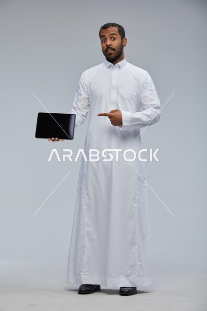 رجل سعودي بالثوب الأبيض يحمل جهاز لوحي ذكي
