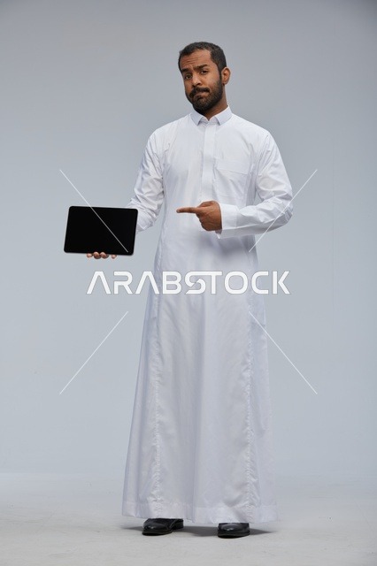 رجل سعودي بالثوب الأبيض يشير إلى جهاز لوحي