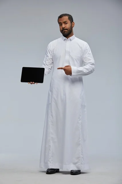 رجل سعودي بالثوب الأبيض يشير إلى جهاز لوحي