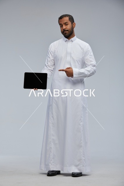 رجل سعودي بالثوب الأبيض يمسك بجهاز لوحي إلكتروني