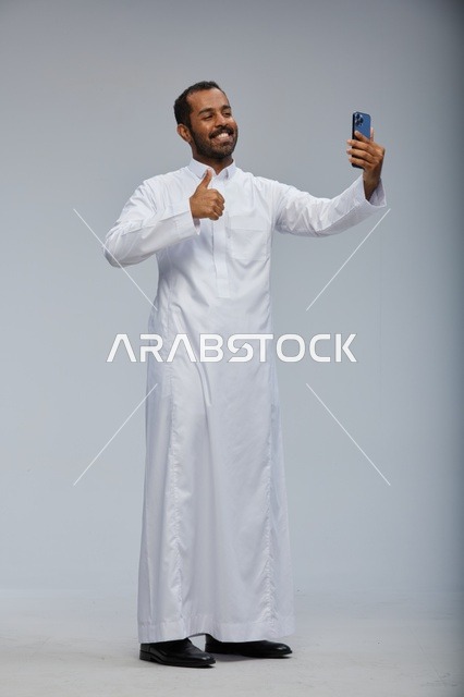 رجل سعودي بالثوب الأبيض يلتقط سيلفي بالهاتف الذكي