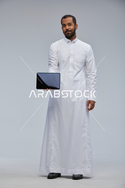 رجل سعودي بالثوب الأبيض يحمل جهاز لوحي