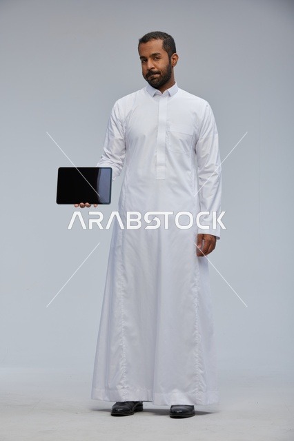 رجل سعودي بالثوب الأبيض يحمل جهاز لوحي في استوديو