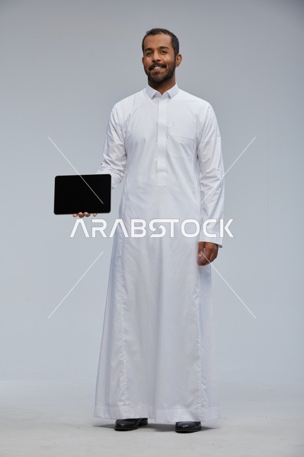 رجل سعودي بالثوب يحمل جهاز لوحي في الاستوديو