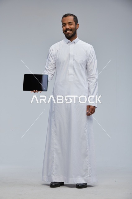 رجل سعودي بالثوب الأبيض يحمل جهاز لوحي في الاستوديو