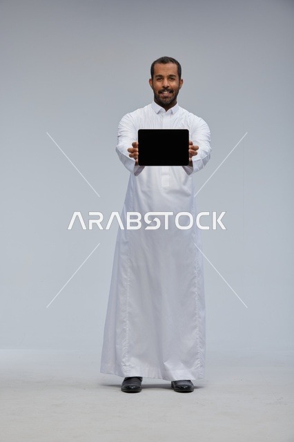 رجل سعودي بالثوب الأبيض يمسك بجهاز لوحي في الاستوديو