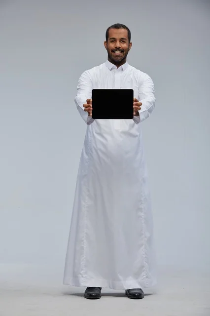 رجل سعودي بالثوب الأبيض يحمل جهازاً لوحياً رقمياً