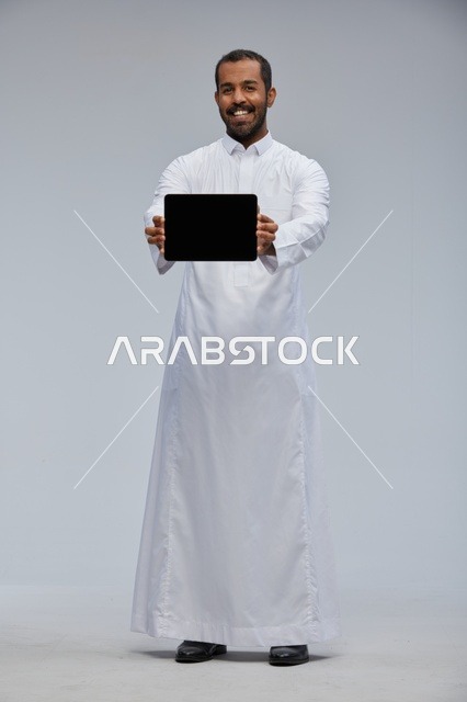 رجل سعودي بالثوب التقليدي يمسك جهاز لوحي شاشة سوداء