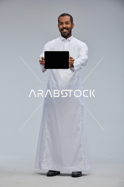 رجل سعودي بالثوب الأبيض يعرض جهازاً لوحياً