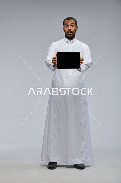 رجل سعودي بالثوب التقليدي يحمل جهاز لوحي في الاستوديو