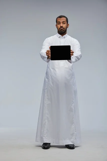 رجل سعودي بالثوب الأبيض يحمل جهازاً لوحياً رقمياً