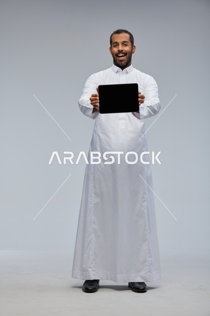 رجل سعودي بالثوب الأبيض يحمل جهازاً لوحياً