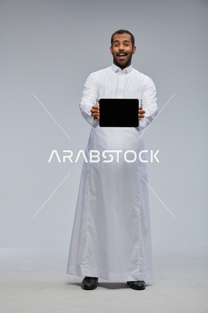 رجل سعودي بالثوب الأبيض يمسك جهاز لوحي في الاستوديو
