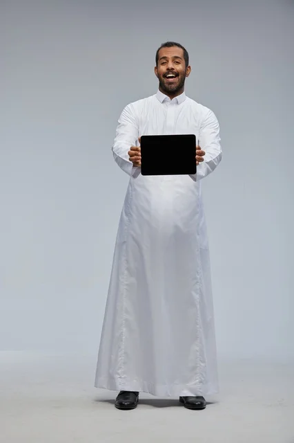 Saudi Man in White Thobe Holding Digital Tablet