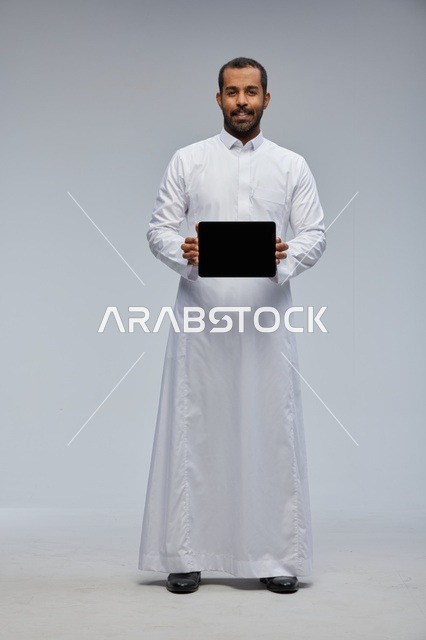 رجل سعودي بالثوب الأبيض يحمل جهاز لوحي