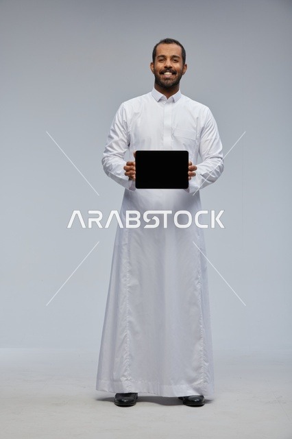 رجل سعودي بالثوب الأبيض يحمل جهاز لوحي في الاستوديو