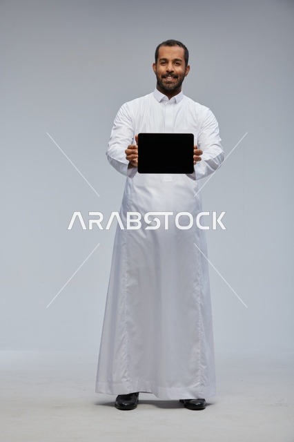 رجل سعودي بثوب أبيض يعرض جهازًا لوحيًا