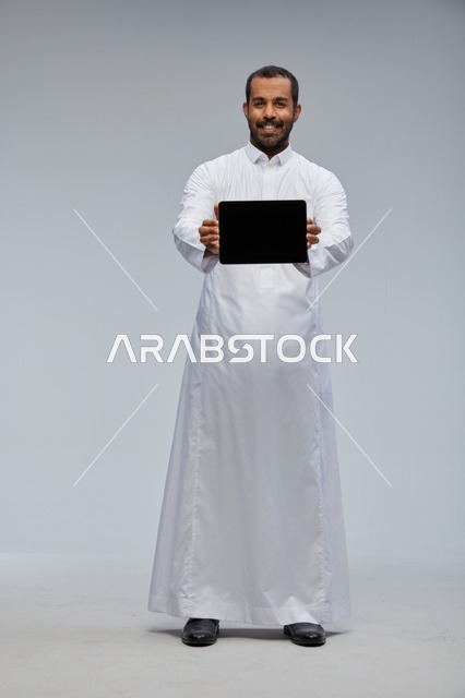 رجل سعودي بالثوب الأبيض يعرض جهاز لوحي