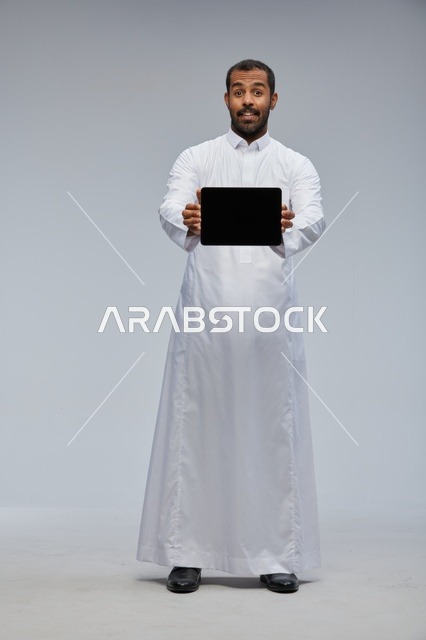 رجل سعودي بالثوب التقليدي يحمل جهاز لوحي في استوديو