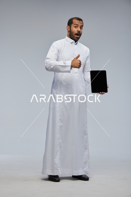 رجل سعودي بالثوب يحمل جهاز لوحي مع إشارة الإعجاب